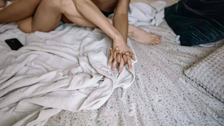Pár se drží za ruce v posteli před prvním sexem